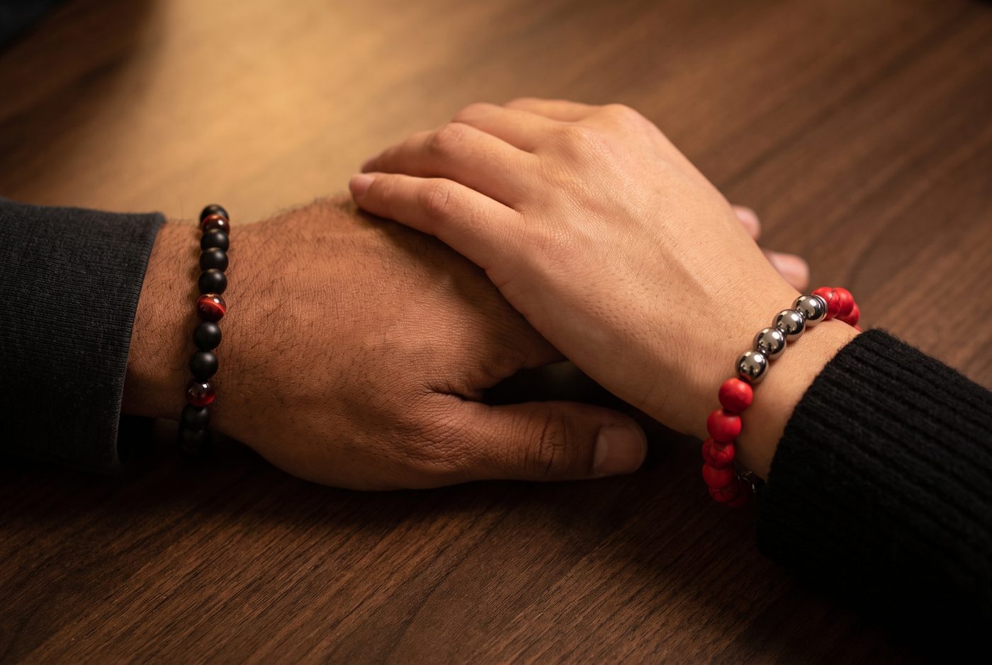 Two hands resting together, one wearing the Ember Onyx bracelet and one wearing the Half and Half bracelet
