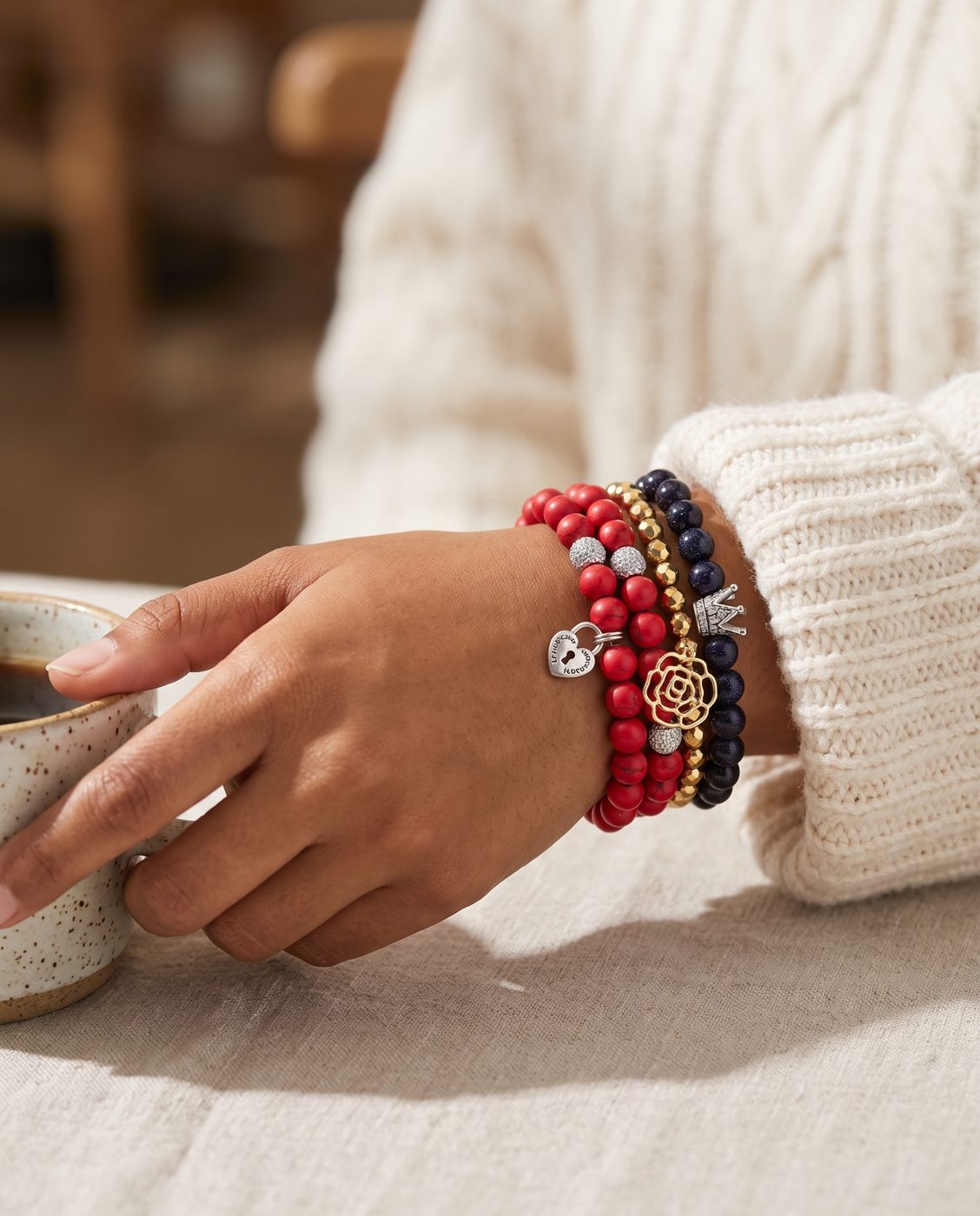 Woman's wrist wearing a stack of Heart Lock Wrap, Gilded Rose and Midnight Goldstone bracelets